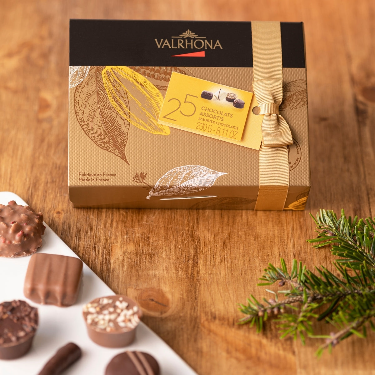 Ballotin de chocolat assortis de 230 gr fermé sur une table et quelques chocolats à côté 